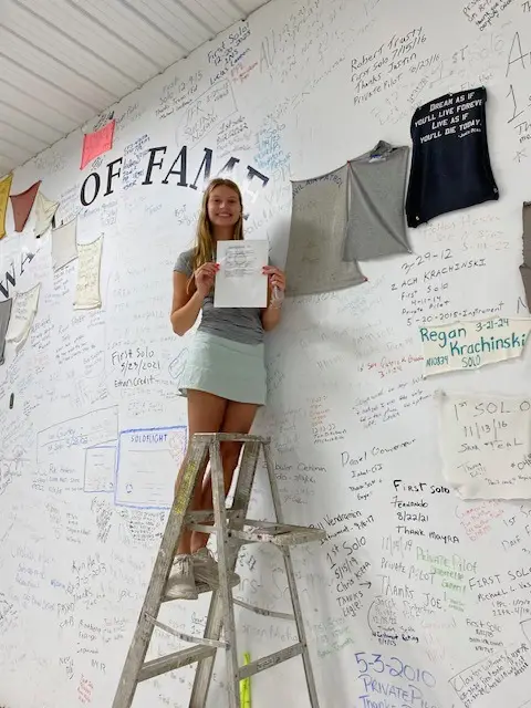 Student on stairs in front of Wall of Fame with certificate